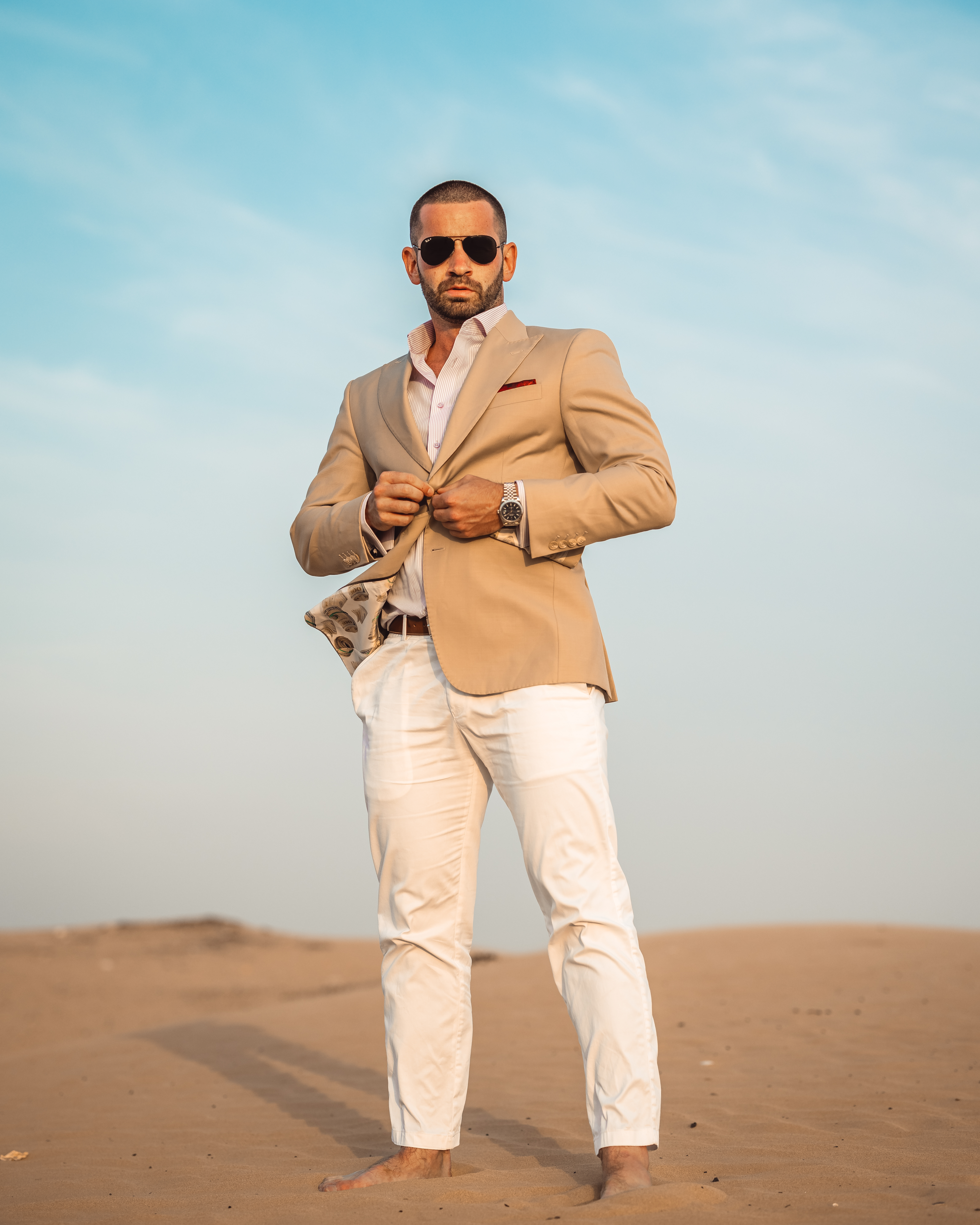 Daniel Kelly wearing a tan suit, standing barefoot on a sand dune