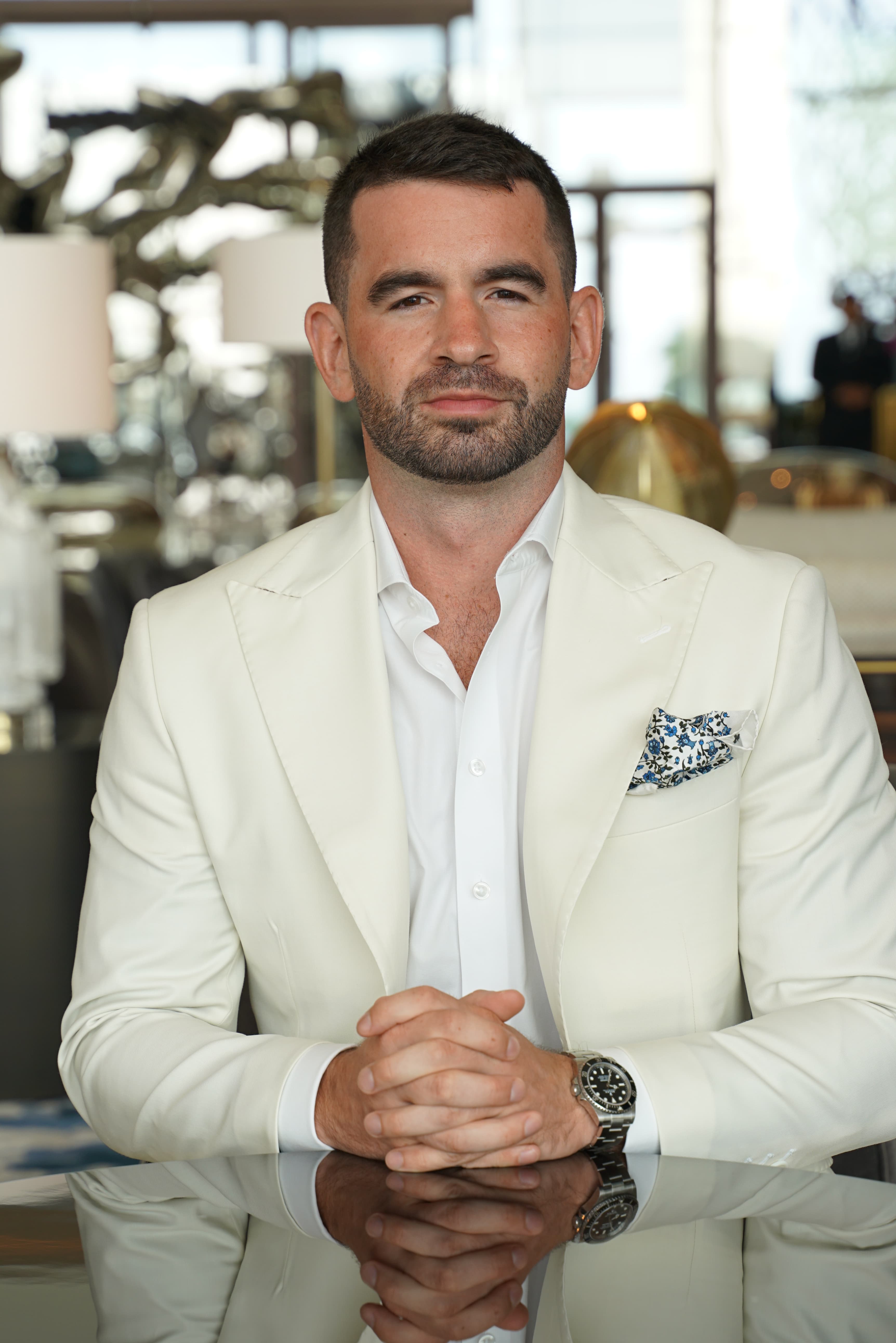 Daniel Kelly wearing a cream-color sports jacket and button-up shirt, sitting across a table